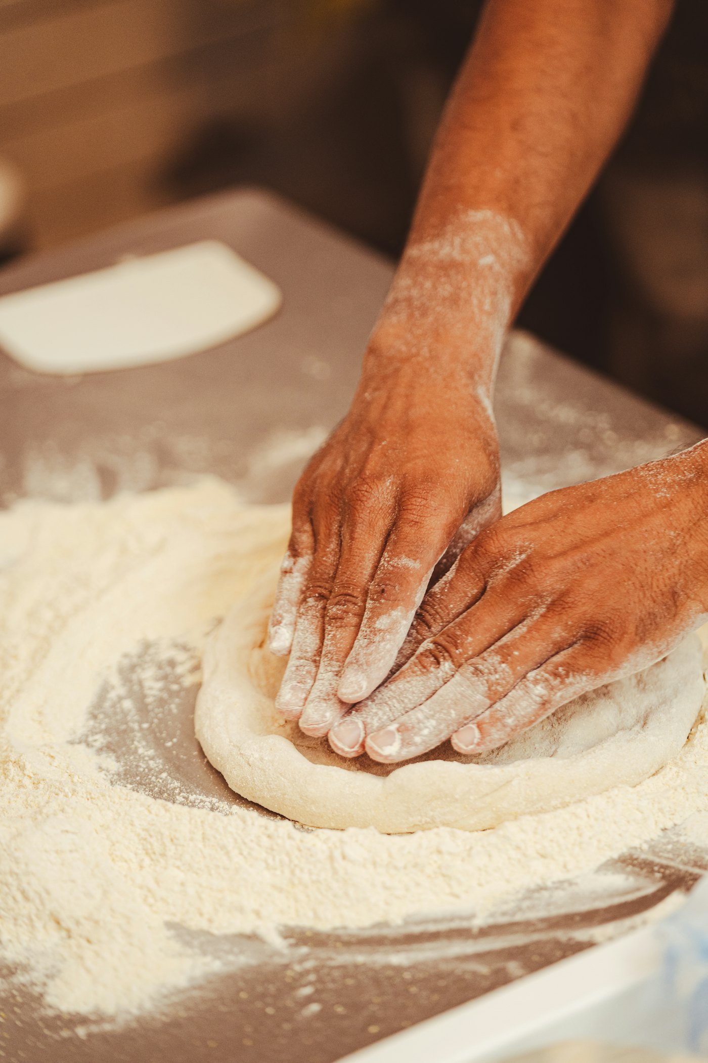 Mãos abrindo a massa de pizza sobre a bancada enfarinhada